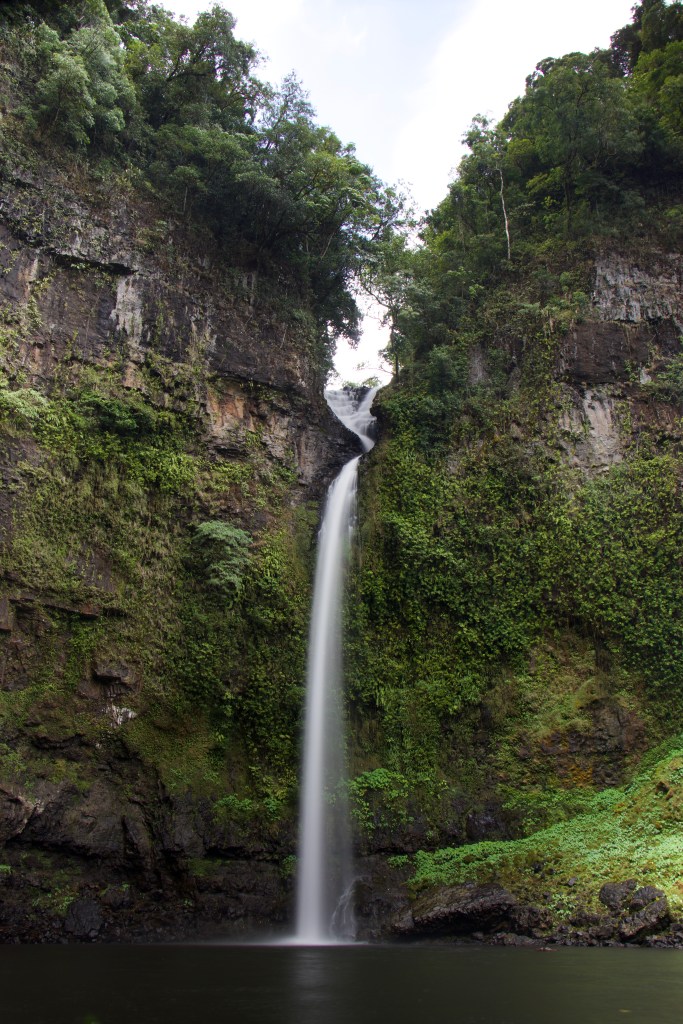 The thin water of Nandroya falls flowing between two large rocks down into the swimming hole below.