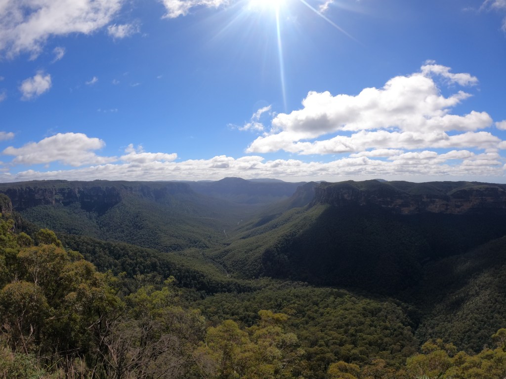A valley of green through the Blue Mountains, bright blue skies with fluffy white clouds. 