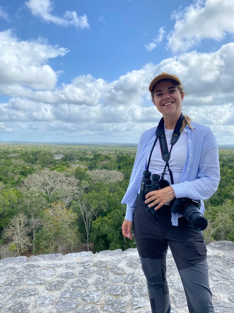 Smiling traveler looking at the camera while standing on top of a Mayan pyramid at Calakmul ruins, Campeche, Mexico.